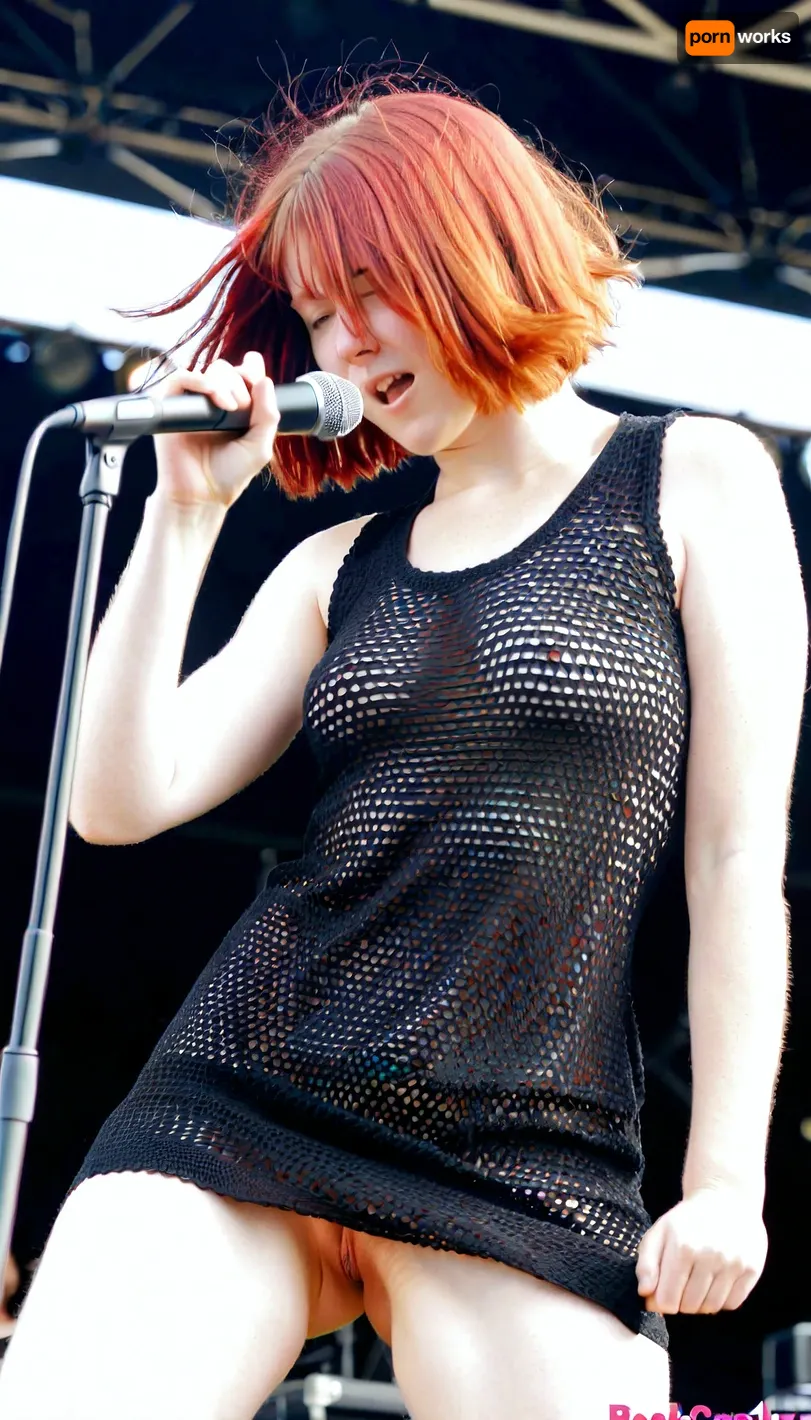 Sexy redhaired, (bobcut), wearing a black coarsely crocheted summer dress, shaking her head, rockband singer pushes her microphone in her pussy on stage during a sunny concert