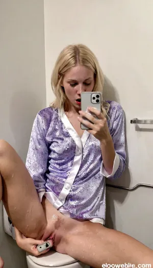 Uma garota loira sueca em um banheiro de um bar de disco está se masturbando enquanto observa seu celular. Ela tem intensa expressão de orgasmo em seu rosto e está vestindo uma camisa branca com jeans azuis