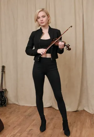 Full body shot, 28 year old Irish American woman, chin-length short blonde hair, blue eyes, chubby cheeks, very pale skin, thin but soft body, small breasts, small waist, black clothes, black crop top, black jacket, black skintight leggings, holding a violin, standing backstage at a concert