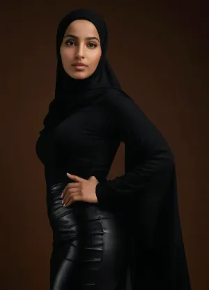 "An ultra-realistic image of a young Arab Algerian woman from Oran, her formal hijab tightly and neatly wrapped around her head, framing her soft, rounded face with high cheekbones, almond-shaped eyes, and a warm complexion reflecting her Oran heritage. Her full, voluptuous body is completely visible from behind, with an ultra-mini black leather skirt that barely covers her hips, exposing much of her lower body. The contrast between her modest hijab and the exposed, curvy contours of her figure creates a striking balance. She wears sleek stiletto heels that elongate her legs, enhancing her bold posture. The scene is lit with professional studio lighting, where the softbox creates a lifelike glow that highlights the texture of her skin, the sheen of the black leather, and the soft folds of her hijab. Every detail—from the contours of her curves to the reflections of light on her exposed skin—is captured with stunning precision, offering a hyper-realistic depiction of beauty, sensuality, and cultural elegance."