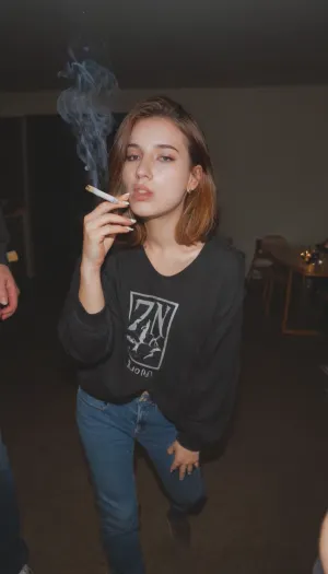 introvert grunge girl at college party in 1992, fully clothed, (while holding a cigarette), smokinglora, <lora:smoking_v2:.7>, <lora:EnvyZoomSliderXL01:-1>