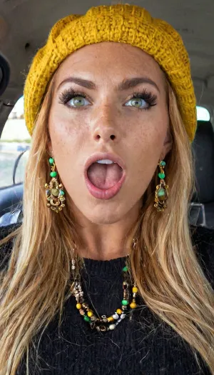 La fille avec la grande bouche et les rousseurs est prête pour une photo cinématographique d'une fille, portant un béret américain, pull noir, et maquillage. Elle a de hautes lignes de bronzage et des yeux verts parfaits. Ses cheveux longs sont dans un poney