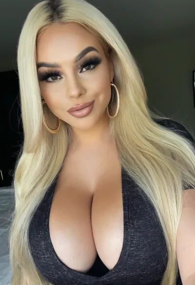 Selfie, headshot, 8k, intricate details. A gorgeous bimbo, looking at viewer, closed mouth, smirk, lipstick, heavy makeup, beautiful long blond hair, huge thick gold hoop earring, graphic eyeliner, thick eyelashes, clothed in bimbo outfit, dark skin, busty, cleavage, <lora:406734_training_data:.5>, <lora:clothed_small:.5>, <lora:1122530_training_data:.6>, <lora:tan-lines-xl-v1:-2>