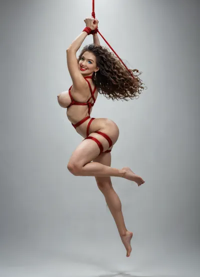 1girl 19 years old, fit, curvy feminine features, extra wide hips, random ethnicity, random hair color, perfect face, (big mile showing teeth), horny smile, green eyes, beauty model, perfect model, high energy, red vivid lipstick, gigantic tits, long legs, Suspension shibari rough sex, rope, black, tape, bondage, soaring pose, side back view, <lora:bdsm_SDXL_1_:.5>, <lora:tiedbreastsblue_XL_reg0_:.5>, <lora:breastclamp_SDXL_reg0_03s:.5>