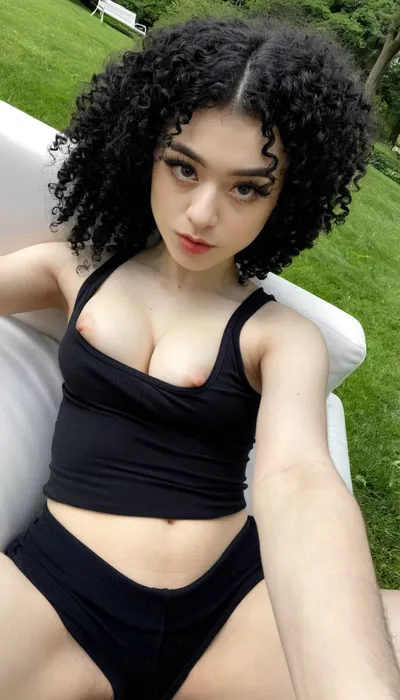 21yo naked girl, medium natural tits, turkish-german mix, black hair, curly hair, long hair, beautiful, high view, selfie, photo taken with iPhone, tight black tank top, selfie on a white couch, in a park