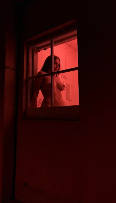 Red light street, in the window of the second floor there is a naked woman with large breasts, view from te glass window, voyeur, <lora:Through_Window_XL-000012:2>, <lora:Window_voyeur:2>