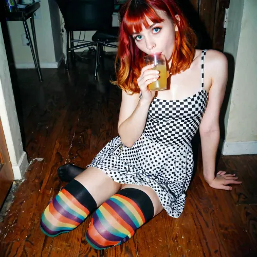 La fille grunge introvertie avec des bangs et des bas multicolores et une jolie robe courte en coton est assise sur le sol dans un coin sombre buvant de la limonade d'un verre à une fête en 1997, en arrière-plan