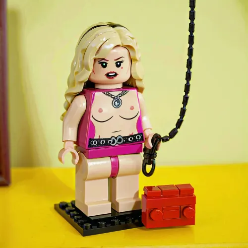 Модель BDSM с белоснежными волосами, в розовом костюме Dominatrix, держит хлыст и цепи в руке. Она окружена такими аксессуарами, как клыки, кнуты и цепи. Картина сопровождается текстом, который читает 